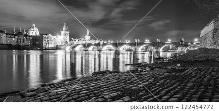 The captivating Charles Bridge stands illuminated against the night sky, reflecting beautifully in the calm waters of the Vltava River. The historic cityscape of Prague glows nearby. 122454772