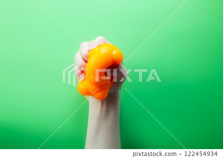 Hand squeeze orange stress ball on green background. Positive thinking concept Hand squeeze orange stress ball on green background. Positive thinking concept 122454934