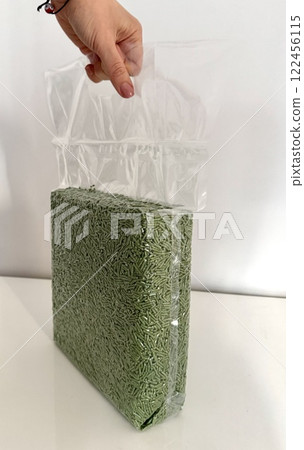 Female hand holding a transparent plastic bag with tofu litter pellets in green palette. Flushable Clumping Fast Drying Tofu Cat Ultra Absorbent Litter Pack. Premium eco litter, soluble in water. 122456115