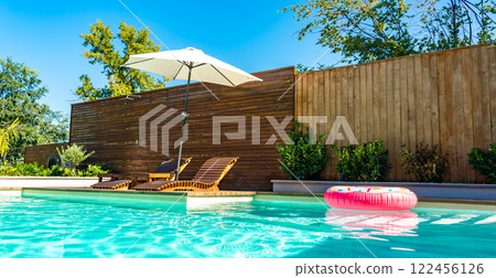 Backyard swimming pool with turquoise water, lounge chairs, umbrella, wooden deck, and pink inflatable ring 122456126