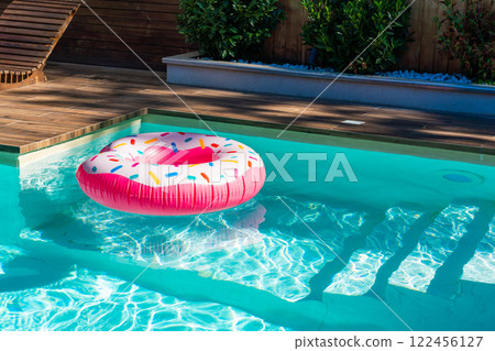 Pink donut inflatable float in turquoise swimming pool with submerged steps and wooden deck Pink donut inflatable float in turquoise swimming pool with submerged steps and wooden deck 122456127