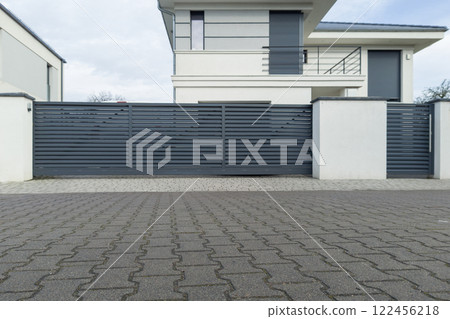 A contemporary house with a sleek sliding metal gate and a paved driveway in a residential area 122456218