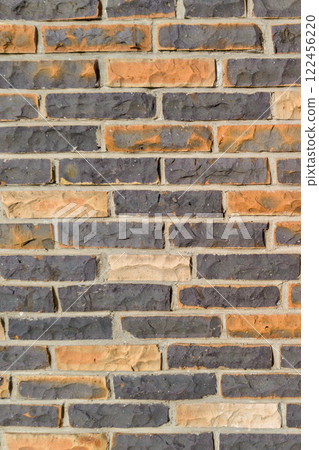 A close up view of a textured brick wall with alternating orange and dark gray bricks creating a unique pattern 122456220