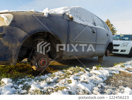 A snowy scene of an abandoned car missing wheels left on blocks highlighting urban issues with neglected vehicles A snowy scene of an abandoned car missing wheels left on blocks highlighting urban issues with neglected vehicles 122456223