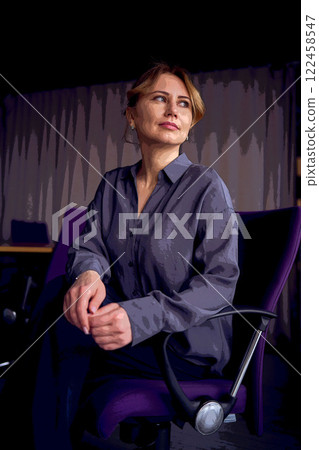 beautiful middle age business woman wearing gray shirt, wide leg pants abd black stilettos sit in purple office chair in modern workspace beautiful middle age business woman wearing gray shirt, wide leg pants abd black stilettos sit in purple office chair in modern workspace 122458547