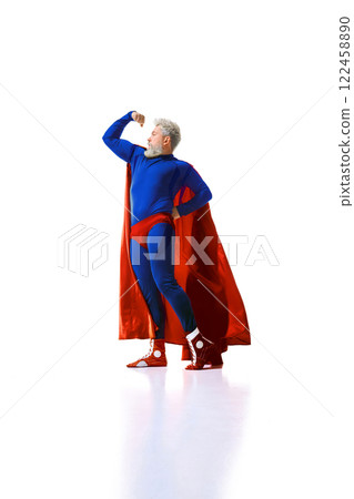 Full-length low-angle view of a bearded man wearing blue superhero costume with red cape, standing in confident pose and showing his strong muscles Full-length low-angle view of a bearded man wearing blue superhero costume with red cape, standing in confident pose and showing his strong muscles 122458890