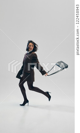 Busy vibes. Stylish businesswoman in motion, in oversized brown blazer, heeled shoes, tights walking with small purse against studio background 122458943