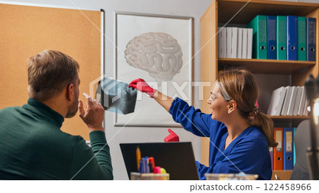 Woman, doctor in blue medical coat sitting at table and looking at x-ray with bearded man, patient. Health check up, medical consultation Woman, doctor in blue medical coat sitting at table and looking at x-ray with bearded man, patient. Health check up, medical consultation 122458966