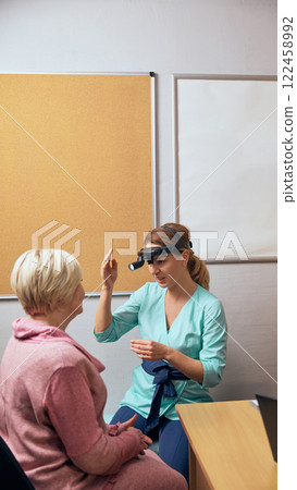 Female doctor closely inspecting elderly woman during medical examination, focusing on skin, facial health, in clinical office environment. ENT Female doctor closely inspecting elderly woman during medical examination, focusing on skin, facial health, in clinical office environment. ENT 122458992