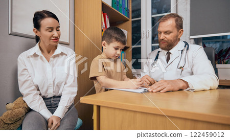 Positive service. Boy, child making notes on table while mother and doctor looking after him. Basic check up for children 122459012