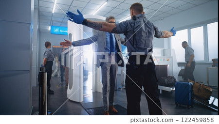 Mature Man Passes Through Metal Detector Scanner. Security Officer Checks Passenger for Plane Flight Mature Man Passes Through Metal Detector Scanner. Security Officer Checks Passenger for Plane Flight 122459858