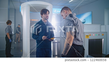 Man Passes Through Metal Detector Scanner. Security Officer Checks Documents, Inspects Passenger Man Passes Through Metal Detector Scanner. Security Officer Checks Documents, Inspects Passenger 122460038