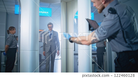 Airport Terminal: Man Passes Through Metal Detector. Security Officer Controls Passenger Inspection Airport Terminal: Man Passes Through Metal Detector. Security Officer Controls Passenger Inspection 122460128
