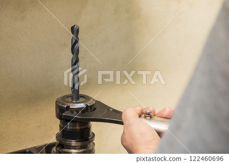 The worker tighten the drill tool to the holder. The worker tighten the drill tool to the holder. 122460696