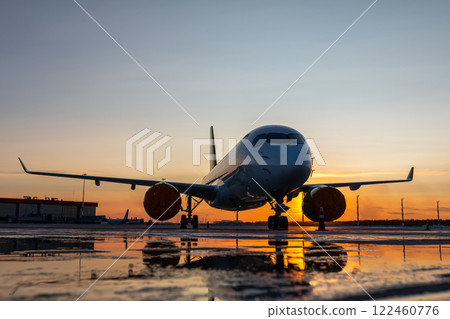 Modern passenger plane on the airport against the backdrop of a scenic sunrise with reflection in a puddle Modern passenger plane on the airport against the backdrop of a scenic sunrise with reflection in a puddle 122460776