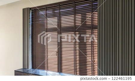 Large wooden blinds on the window in minimalistic interior. Manually operated blinds, 50mm slats with braid ladder. 122461195