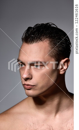Shirtless young brunette man, looks directly forward with confidence against dark studio background. Side view portrait. 122461616