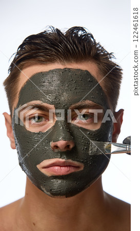 Man with smooth skin looking directly forward, and hand wearing black glove holding brush, mask covering most of face against white studio background. 122461618