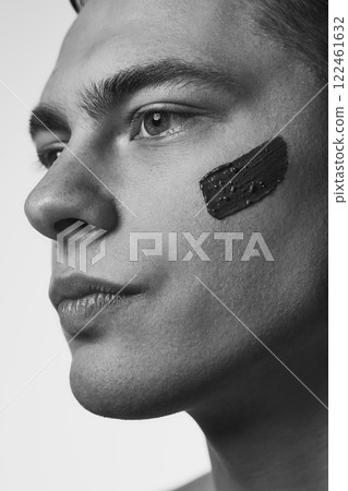 Close up portrait of young attractive man with well-kept, healthy skin looking forward, with nourishment, clay facial mask. Black and white photo. 122461632