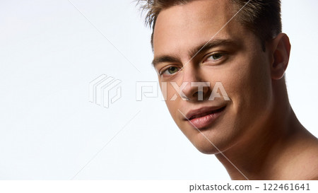Confident young attractive man with wet hair, looking at camera with light smile against white studio background. Male model with well-kept healthy skin. 122461641