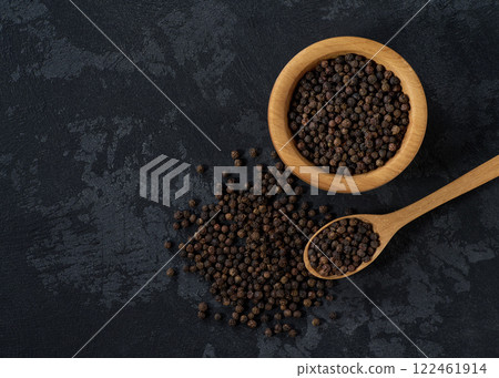 black pepper seeds in a wooden bowl on a black stone table, top view. black pepper seeds in a wooden bowl on a black stone table, top view. 122461914