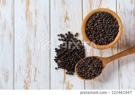 wooden bowl with black peppercorns on a light kitchen table, top view. 122461947