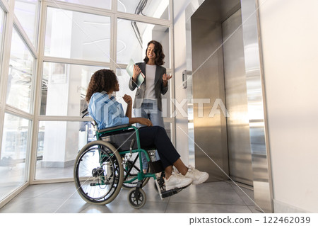Disabled woman in wheelchair presses waiting the elevator with female colleague in the office 122462039