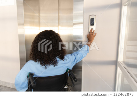 Woman sitting on wheelchair and pushing sensor button for call the elevator in office 122462073