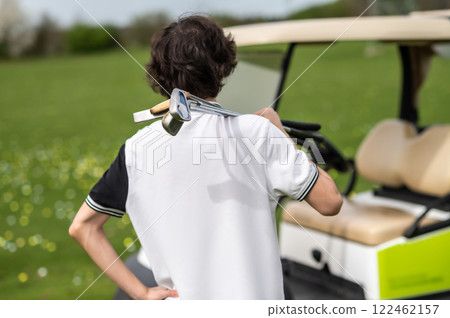Dark-haired young golfer near the golf cart with brassie Dark-haired young golfer near the golf cart with brassie 122462157