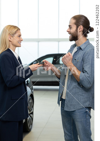 Young male customer talking to a consultant in a car showroom Young male customer talking to a consultant in a car showroom 122462202