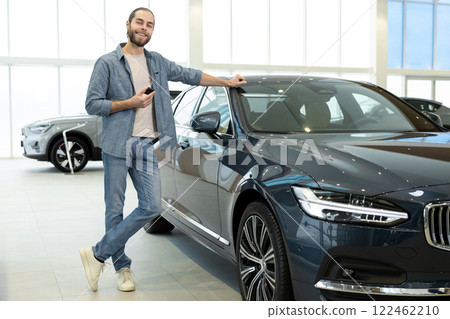 Confident caucasian young man standing near a new car in a car showroom Confident caucasian young man standing near a new car in a car showroom 122462210