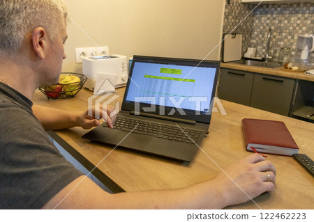 Man working on laptop on the kitchen counter top with an excel sheet on computer screen showing bank loan amortization table. 122462223