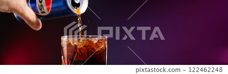 Cola is poured into a glass with ice cubes on a dark background close-up 122462248