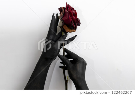 The black hands with long nails hold a rose and make it dry. Concept photo with woman hands painted in black paint with hold a red flower. Demon power in hands make rose die 122462267