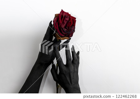 The black hands with long nails hold a rose and make it dry. Concept photo with woman hands painted in black paint with hold a red flower. Demon power in hands make rose die 122462268
