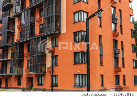Contemporary apartment building with orange facades, featuring numerous balconies with dark-framed windows. Urban housing concept Contemporary apartment building with orange facades, featuring numerous balconies with dark-framed windows. Urban housing concept 122462916