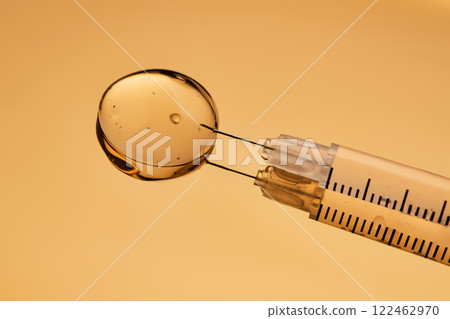 A drop of gel pours from a syringe for cosmetic procedures. 122462970
