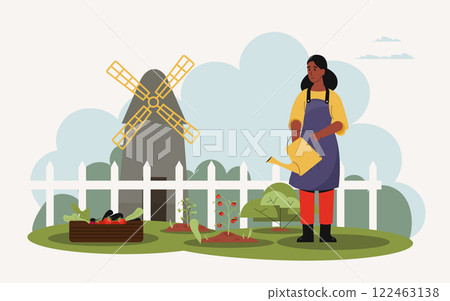 Young woman farmer wearing apron and watering plants in her vegetable garden with tomatoes, lettuce and eggplants growing near a wooden crate and a windmill in background Young woman farmer wearing apron and watering plants in her vegetable garden with tomatoes, lettuce and eggplants growing near a wooden crate and a windmill in background 122463138
