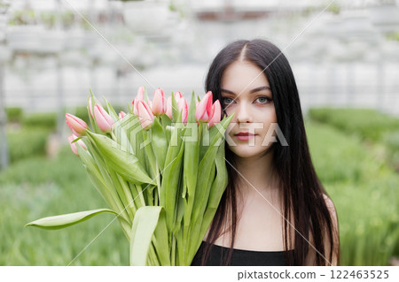 Young woman standing in large greenhouse and holding a blooming tulips in her hands 122463525