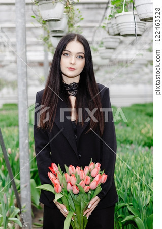 Young woman standing in large greenhouse and holding a blooming tulips in her hands Young woman standing in large greenhouse and holding a blooming tulips in her hands 122463528