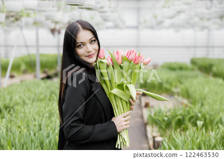 Young woman standing in large greenhouse and holding a blooming tulips in her hands 122463530