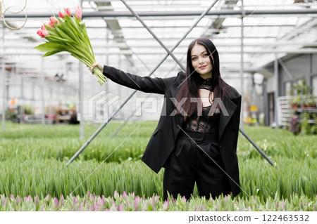 Young woman standing in large greenhouse and holding a blooming tulips in her hands Young woman standing in large greenhouse and holding a blooming tulips in her hands 122463532