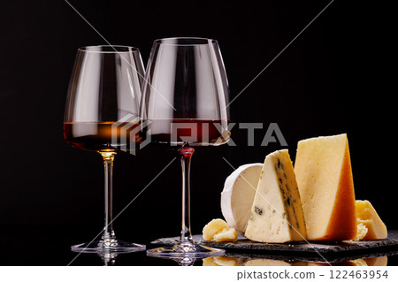 A refined selection of aged cheeses presented on a board, accompanied by a glasses of wine A refined selection of aged cheeses presented on a board, accompanied by a glasses of wine 122463954