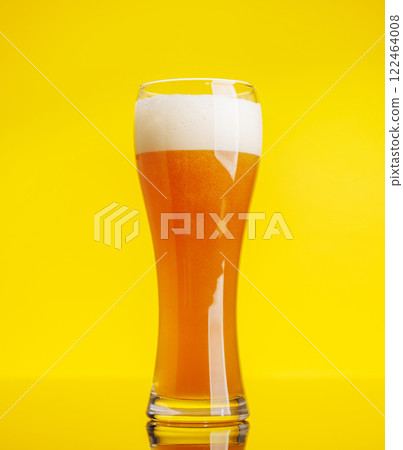 A frothy glass of fresh beer against a bright yellow background 122464008