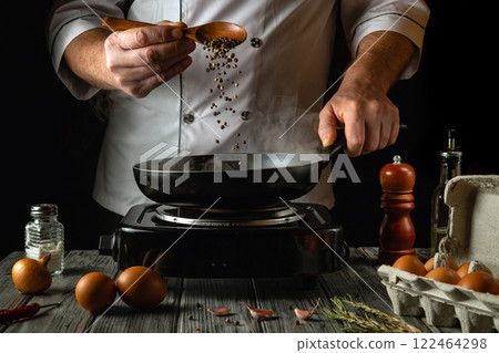 A skilled chef adds fresh peppercorns to a hot pan, releasing aromatic steam. The kitchen is lively with ingredients like eggs, garlic, and herbs, creating a delicious culinary atmosphere A skilled chef adds fresh peppercorns to a hot pan, releasing aromatic steam. The kitchen is lively with ingredients like eggs, garlic, and herbs, creating a delicious culinary atmosphere 122464298
