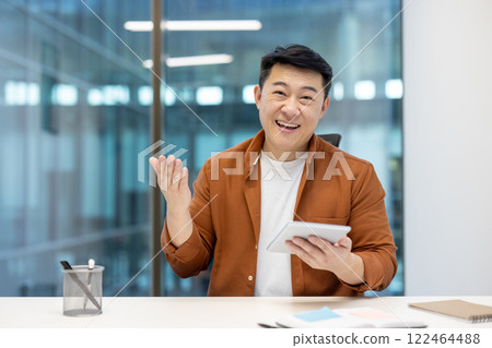 Asian man and mature businessman looking at the camera and communicating during a video call using a smartphone, displaying a cheerful and engaging demeanor in a professional office setting. Asian man and mature businessman looking at the camera and communicating during a video call using a smartphone, displaying a cheerful and engaging demeanor in a professional office setting. 122464488