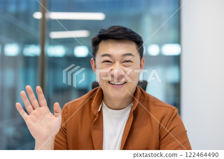 Asian mature businessman on a video call. He smiles genuinely while looking at the camera. 122464490
