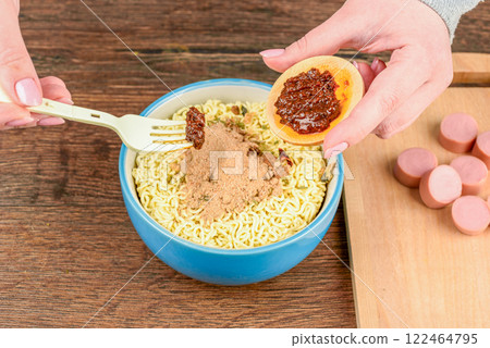 A woman spoons sauce from a saucer on instant noodles using a fork. 122464795
