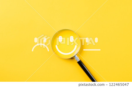 Customer review satisfaction feedback survey concept to gather insights and improve its services. A magnifying glass focuses on smile face among different feedback emoticons on yellow background 122465047