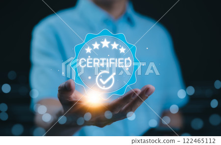 Certified concept. A person holds a glowing holographic badge displaying the word "Certified" with a checkmark and stars, symbolizing quality assurance, accreditation, and validation. ISO Certified, 122465112